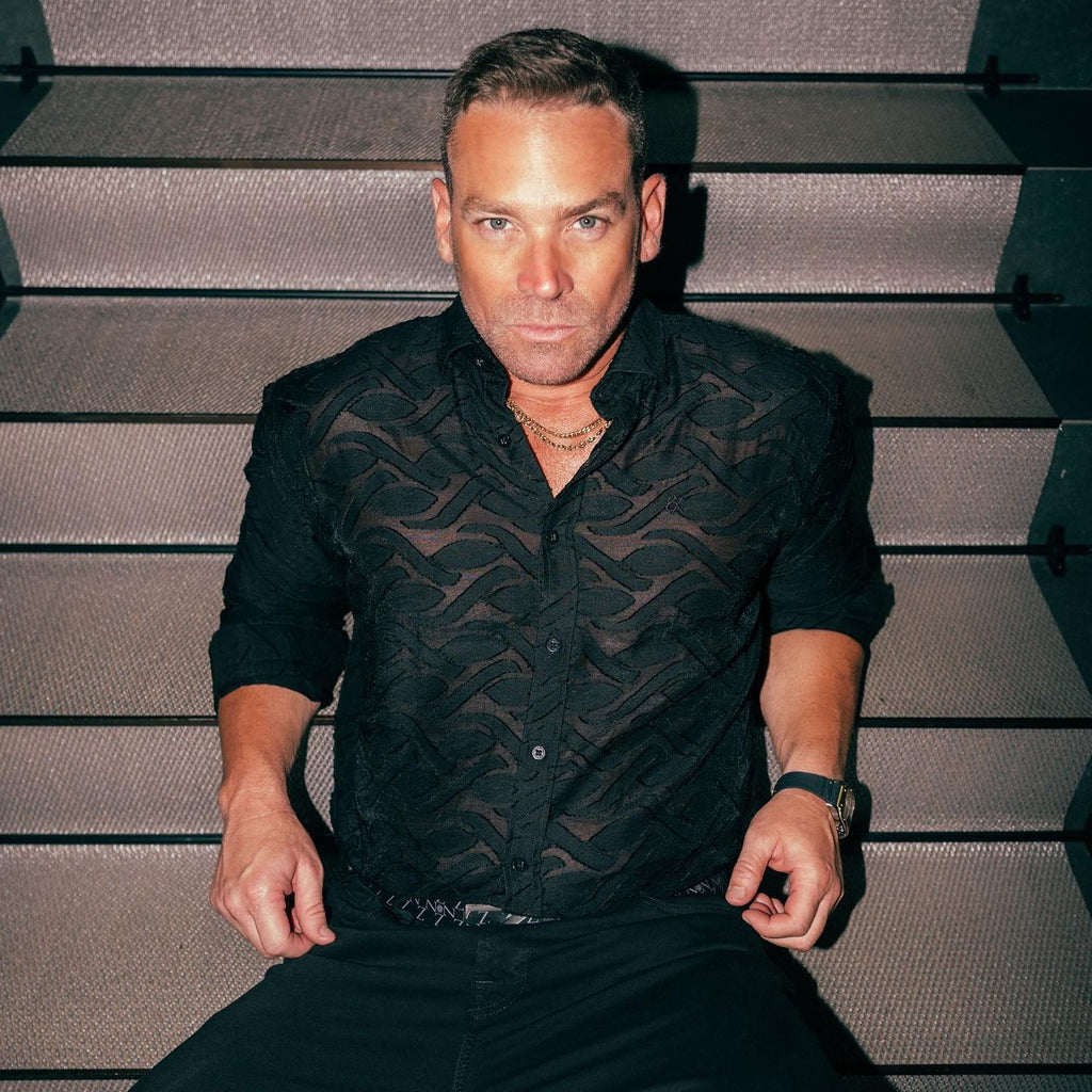model wearing a black sheer jacquard button down shirt while sitting on stairs