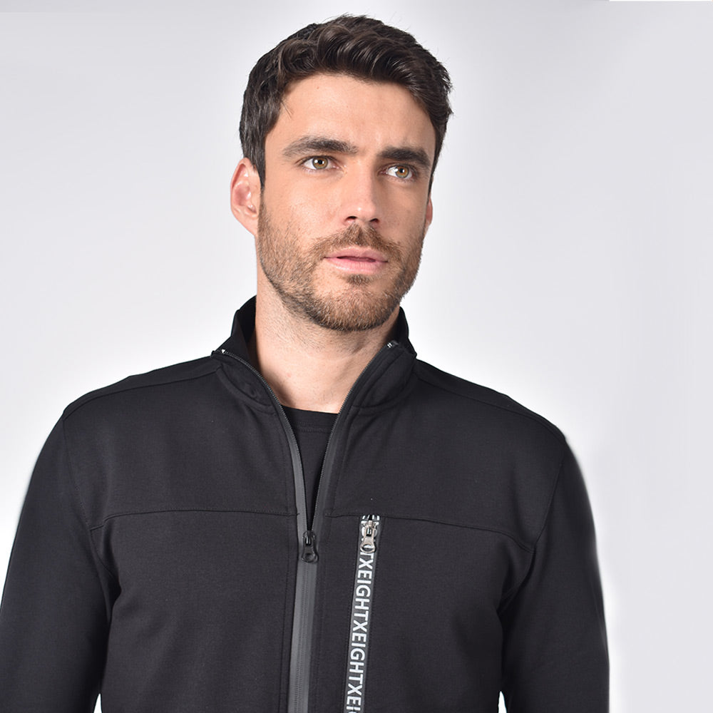Model in black, cotton track jacket with hidden, full front-zipper; grey piping detail; and logo-lined chest zip-pocket.