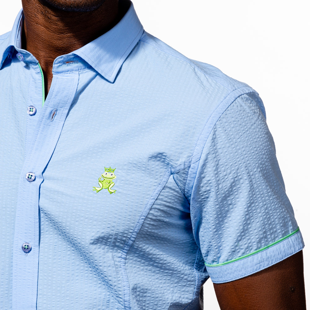 Close up of model in short sleeve, light-blue seersucker button up with green, embroidered frog on chest.