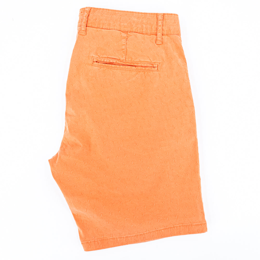 Folded orange shorts with back welt pocket.