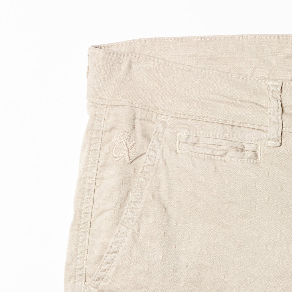 Close-up of beige shorts displaying subtle jacquard texturing and 8x logo embroidery on the right pocket