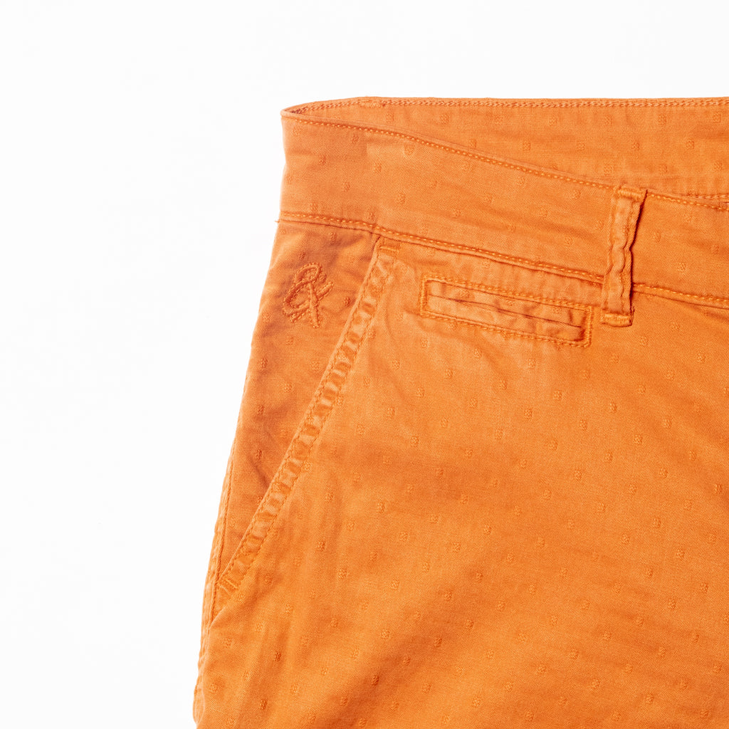 Close-up of orange shorts displaying subtle jacquard texturing and 8x logo embroidery on the right pocket
