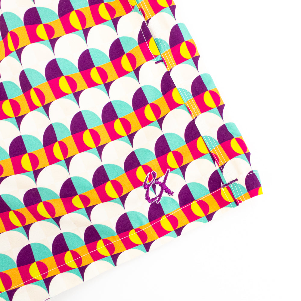 Purples, blue and yellow printed swim trunks. Up close view of embroidered logo.