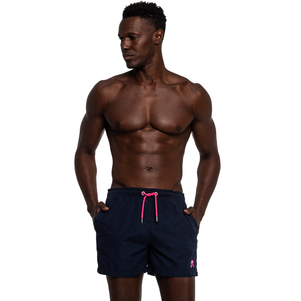 Model wearing navy swim shorts with magenta drawstrings and frog logo
