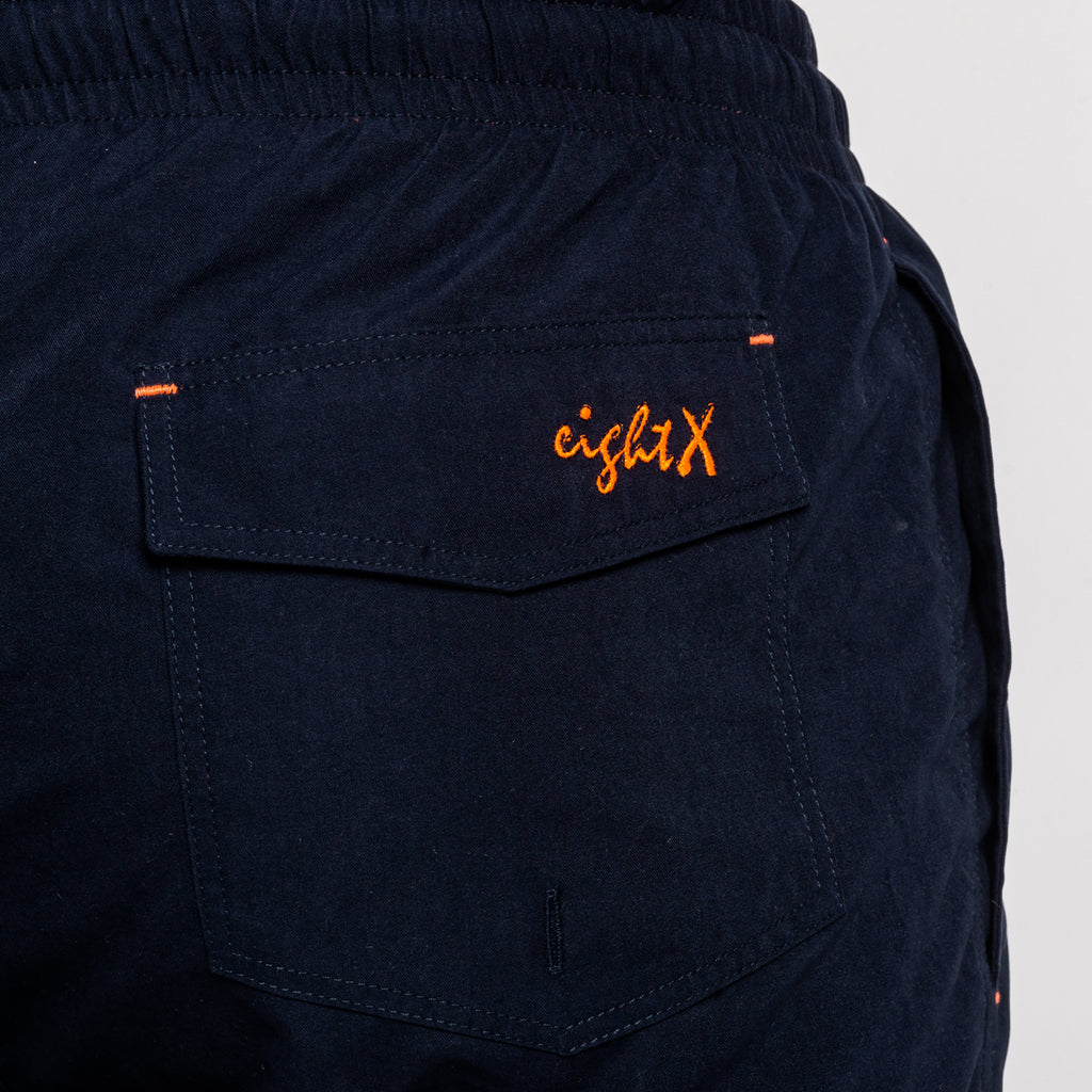 Back of navy swim shorts showing back pocket and a orange Eight X logo on the pocket flap