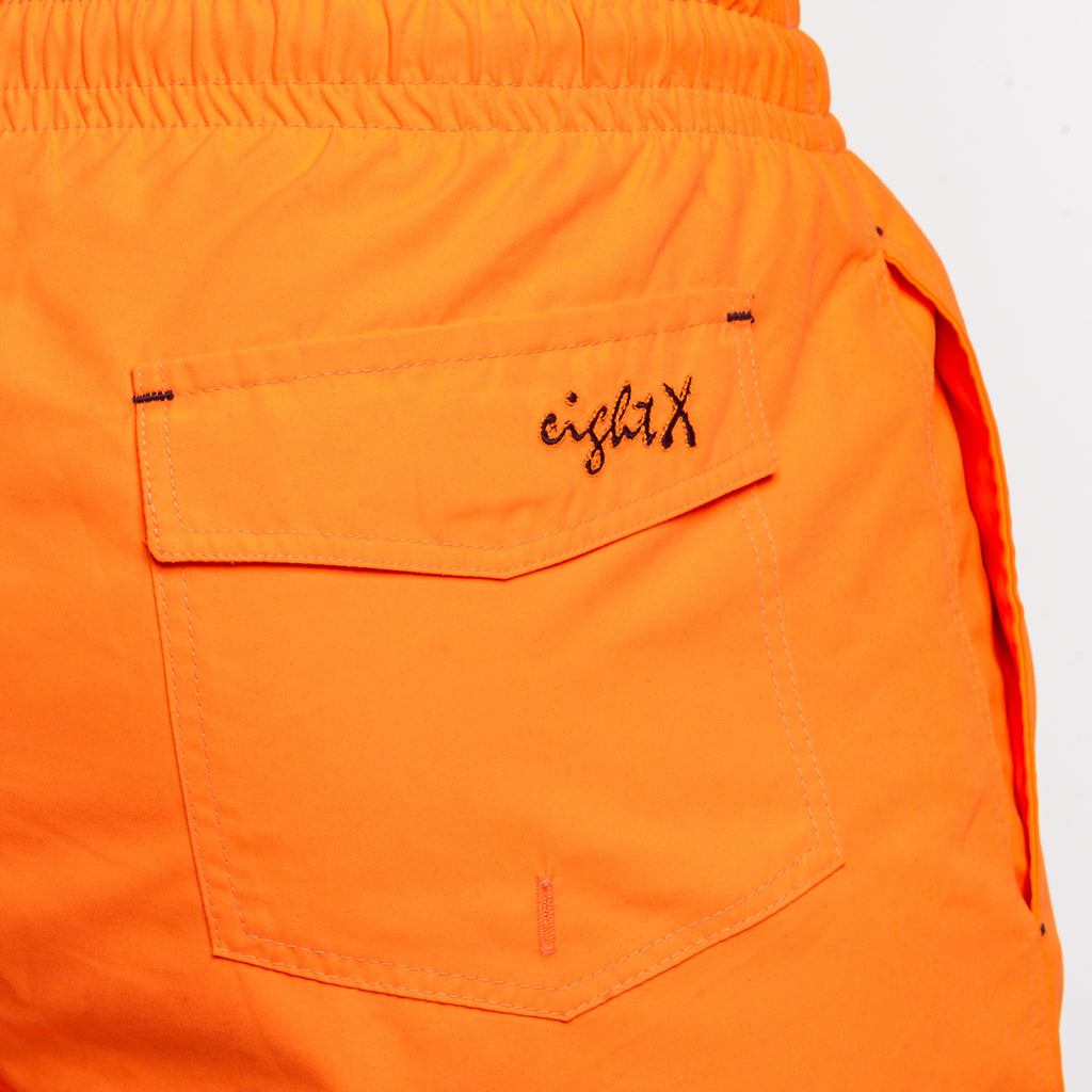 Back of orange swim shorts showing back pocket and a black Eight X logo on the pocket flap