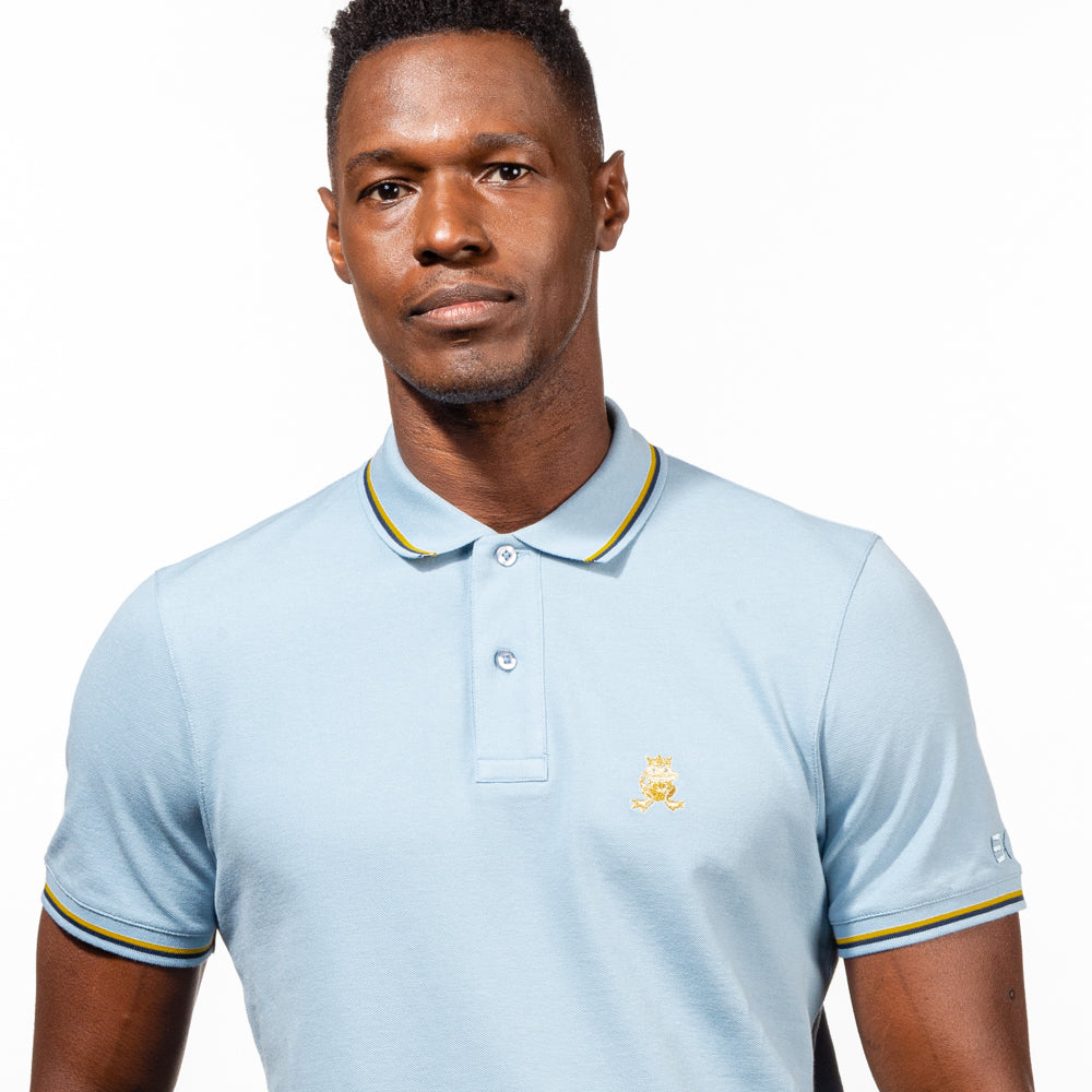 Model in light-blue polo with tipped collar, two-button placket, and striped, ribbed armbands. Featuring embroidered gold frog mascot and embroidered EX Logo on left sleeve.
