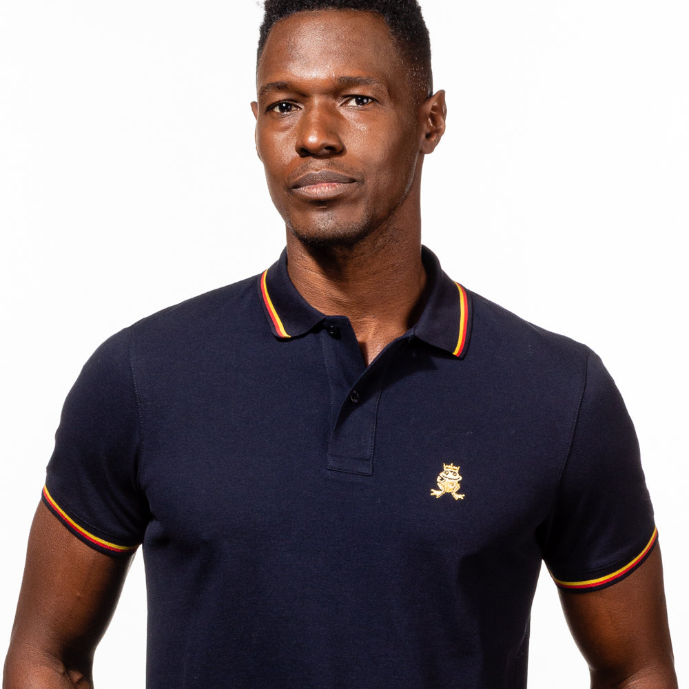 Model in navy-blue polo with tipped collar, two-button placket, and striped, ribbed armbands. Featuring embroidered gold frog mascot.