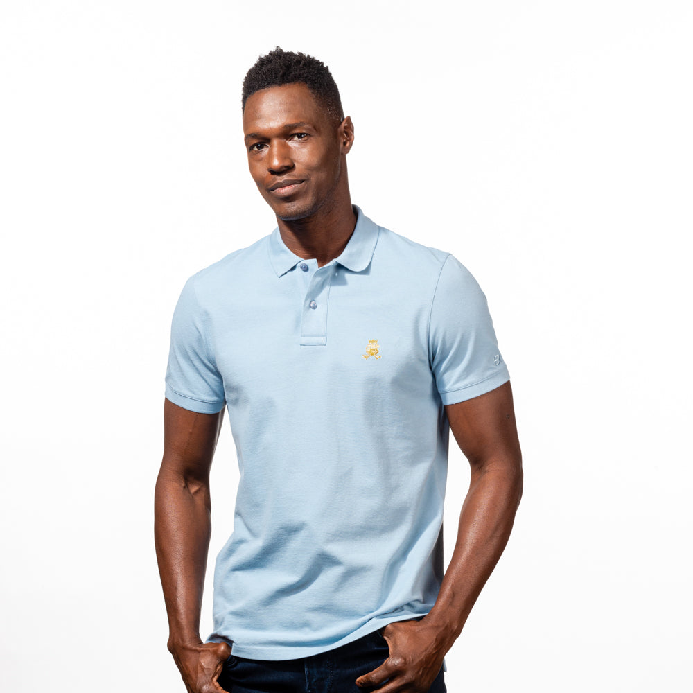 Model in light-blue polo with two-button placket, ribbed armbands, and embroidered gold frog mascot. 