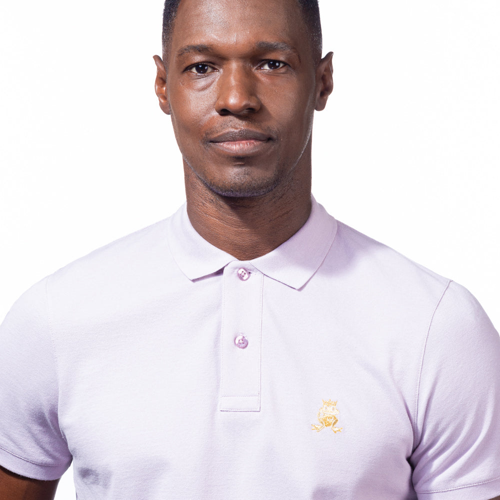 Model in lilac polo with two-button placket, ribbed armbands, and embroidered gold frog mascot. 