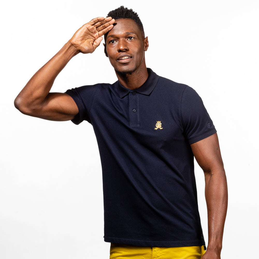 Model in navy polo with two-button placket, ribbed armbands, and embroidered gold frog mascot. 