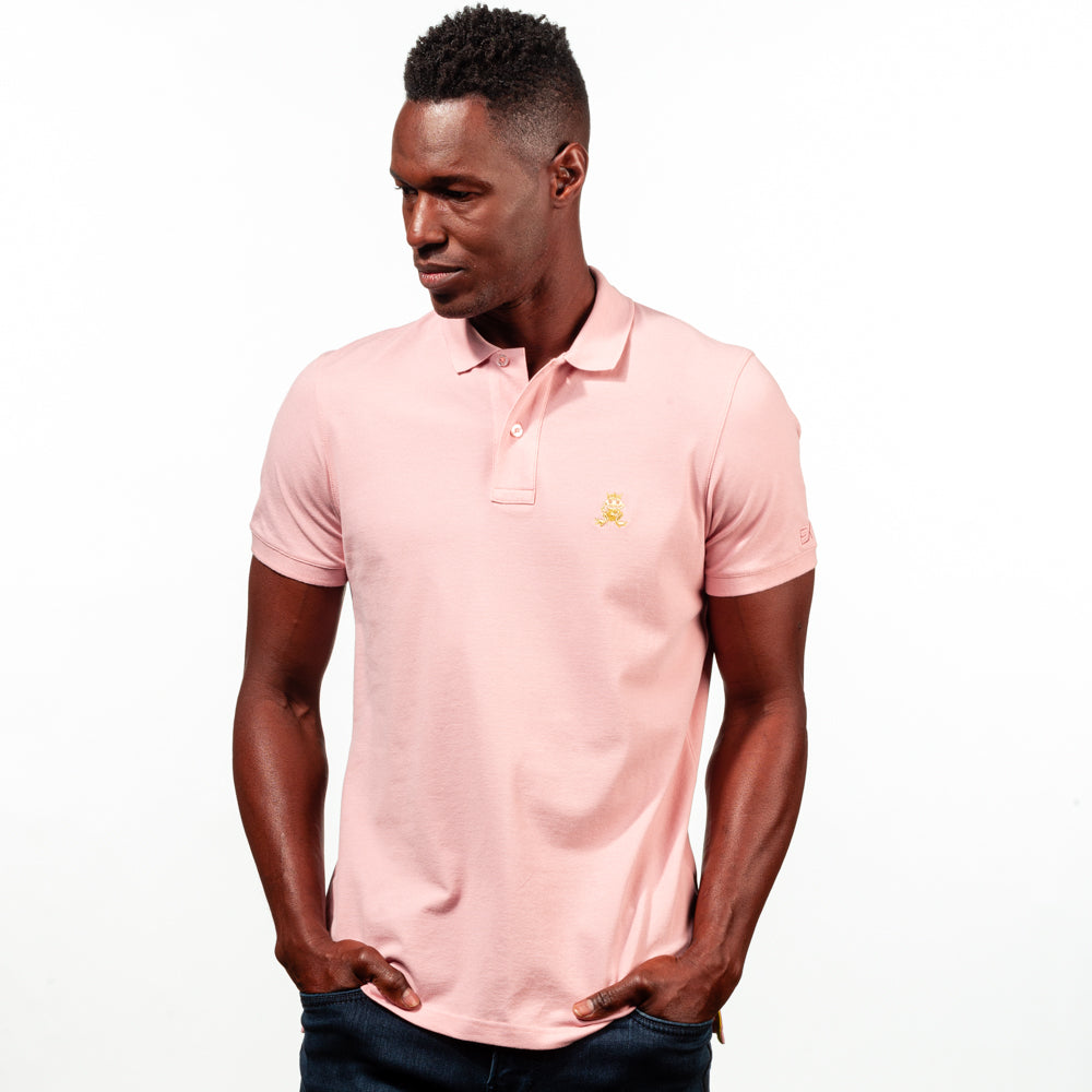 Model in light-pink polo with two-button placket, ribbed armbands, and embroidered gold frog mascot. 